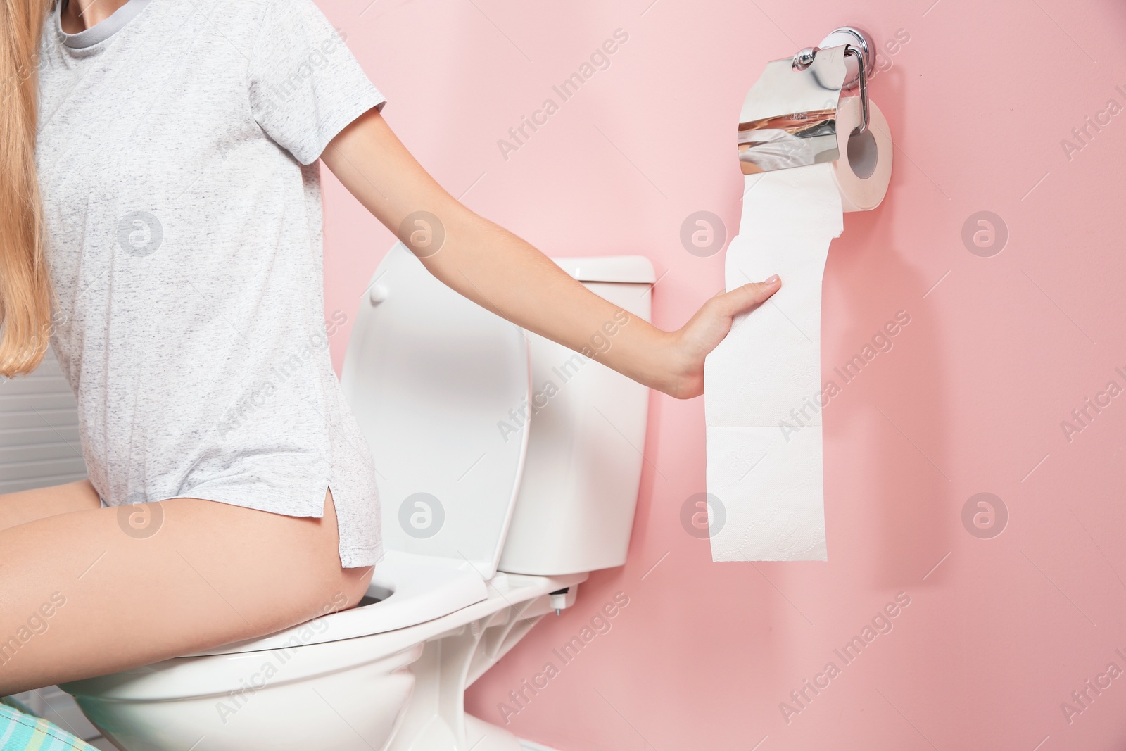 Photo of Woman sitting on toilet bowl and pulling paper in bathroom