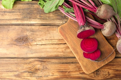 Photo of Cut and whole raw beets on wooden table, flat lay. Space for text
