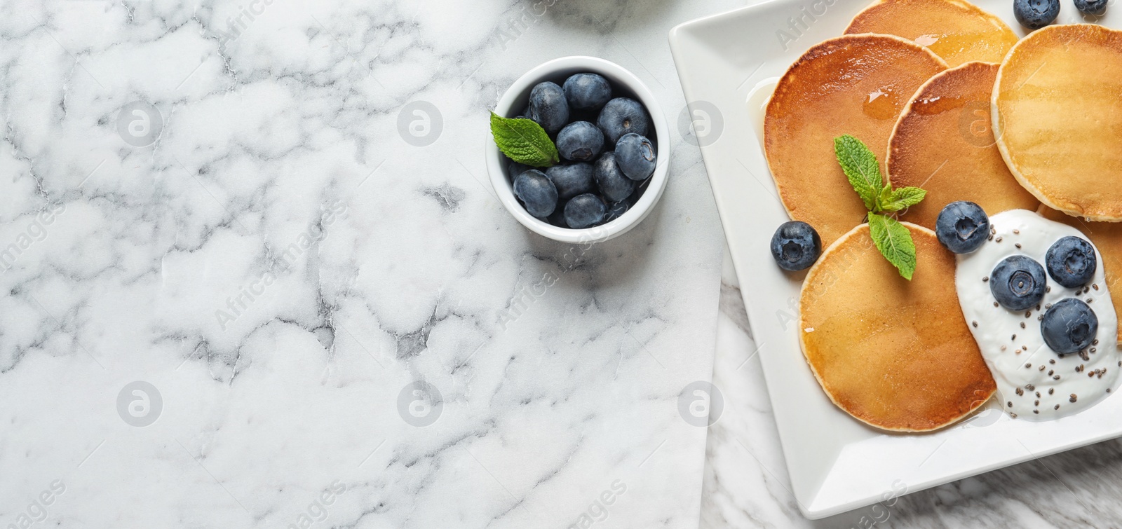 Image of Tasty pancakes with blueberries, sauce and space for text on white marble table, flat lay. Banner design