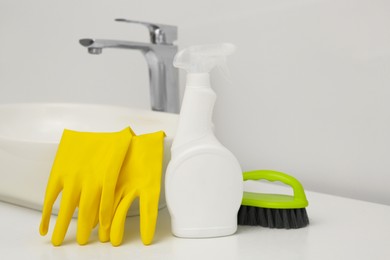 Photo of Spray bottle of cleaning product, rubber gloves and brush near washbasin