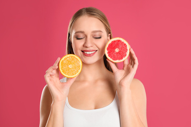 Photo of Young woman with cut orange and grapefruit on pink background. Vitamin rich food