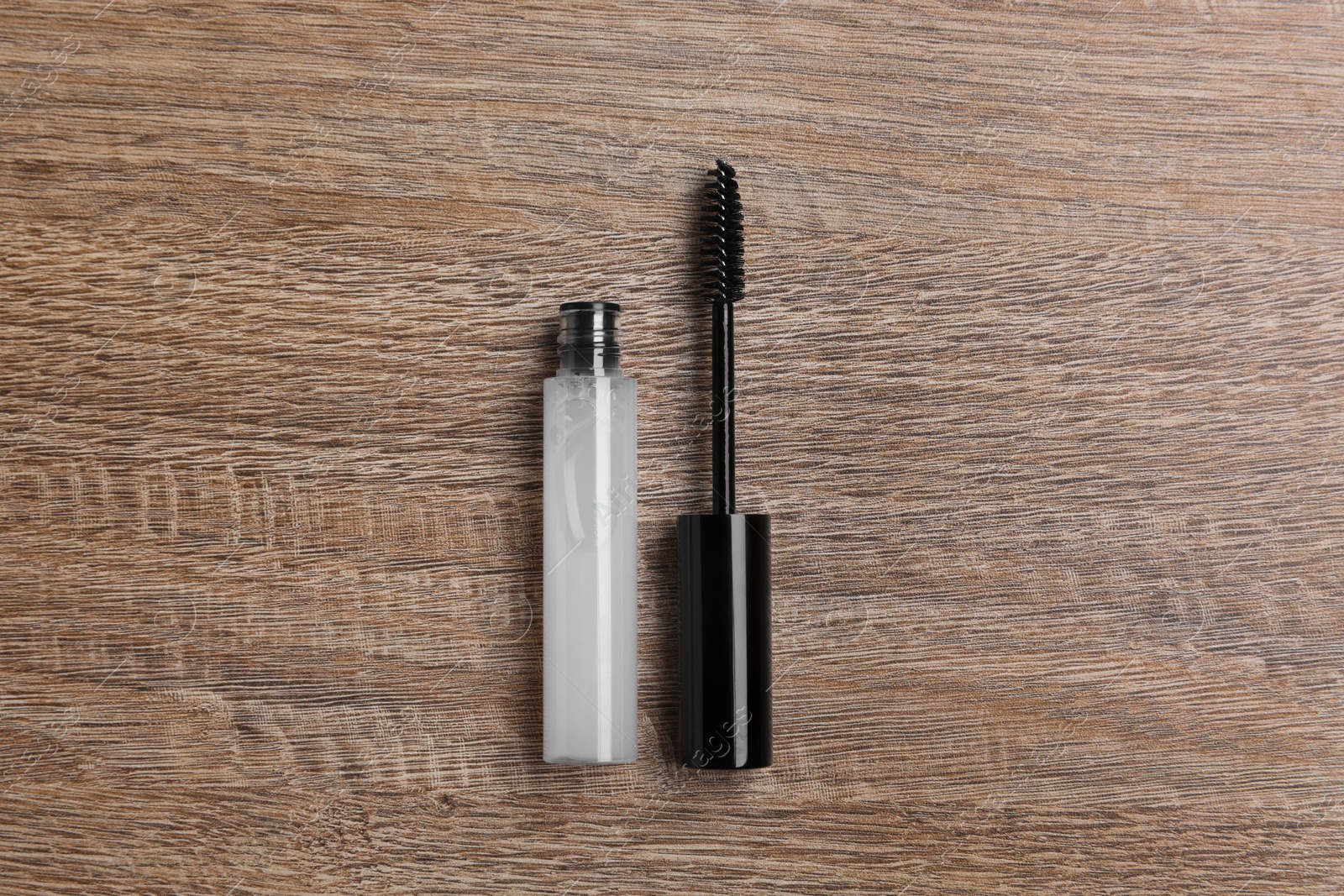 Photo of Tube of eyelash oil and brush on wooden table, flat lay