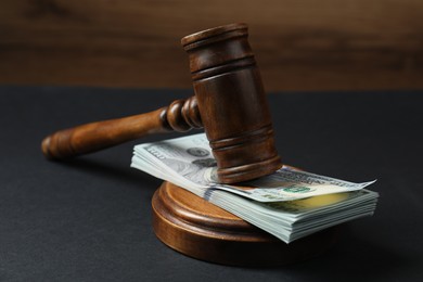 Photo of Law gavel with stack of dollars on black table, closeup