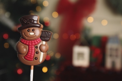 Photo of Funny chocolate snowman candy against blurred Christmas tree, closeup. Space for text