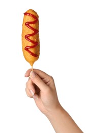 Woman holding delicious deep fried corn dog with ketchup on white background, closeup