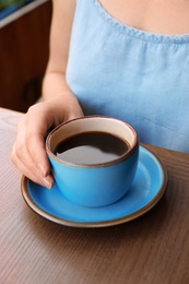 Woman with cup of fresh aromatic coffee at table, closeup