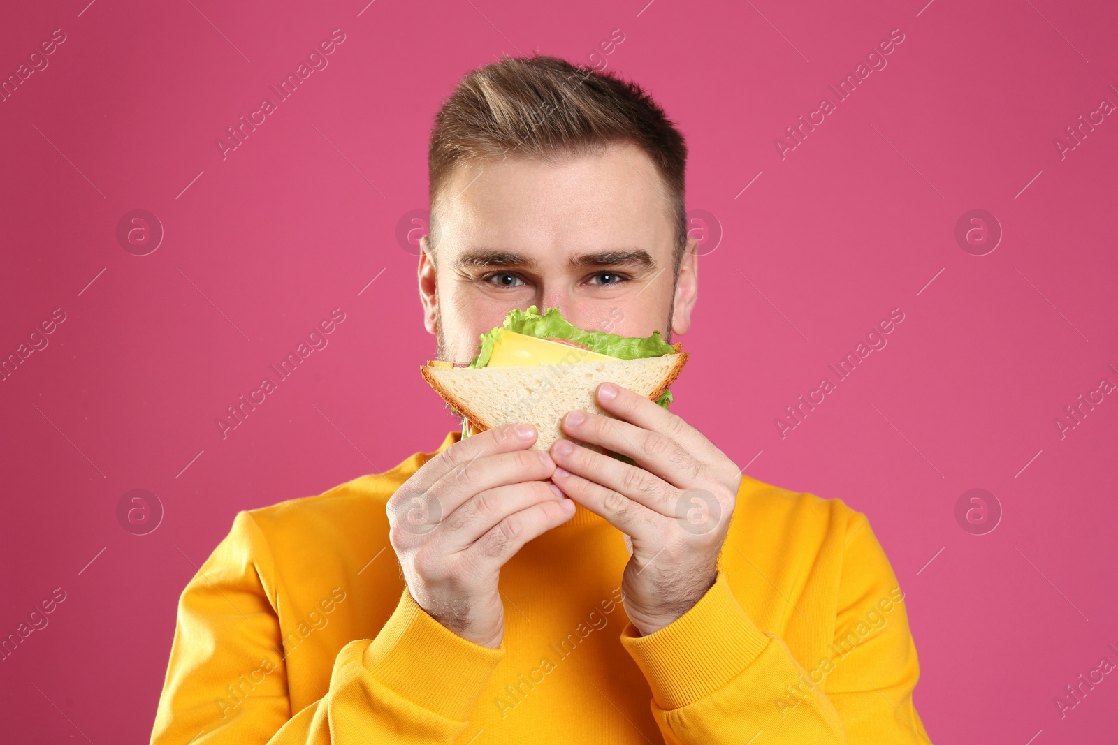 Photo of Young man eating tasty sandwich on pink background