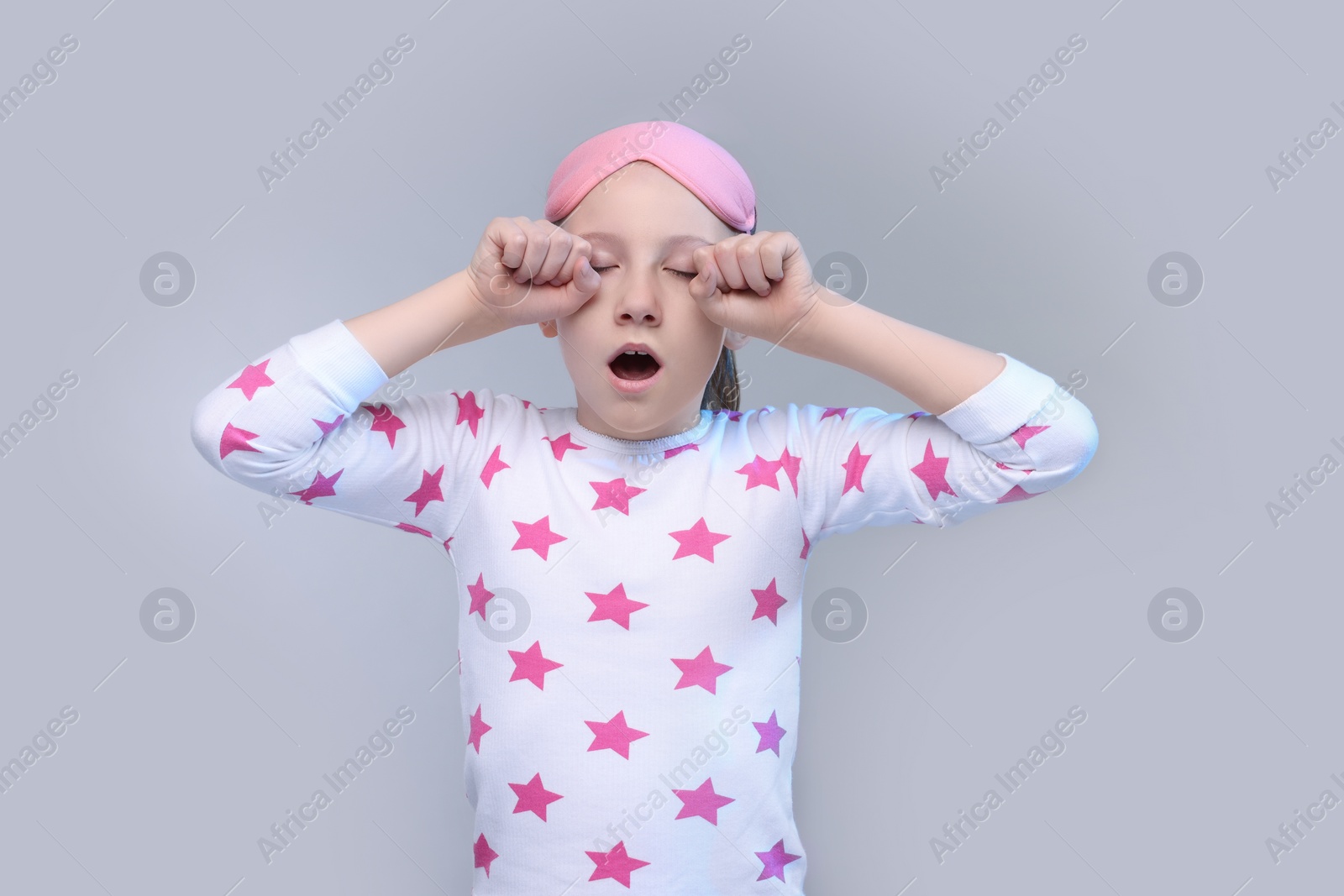 Photo of Girl with sleep mask yawning on light grey background. Insomnia problem