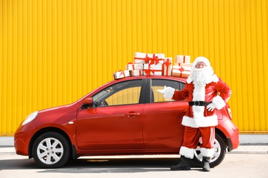 Authentic Santa Claus near red car with gift boxes, outdoors