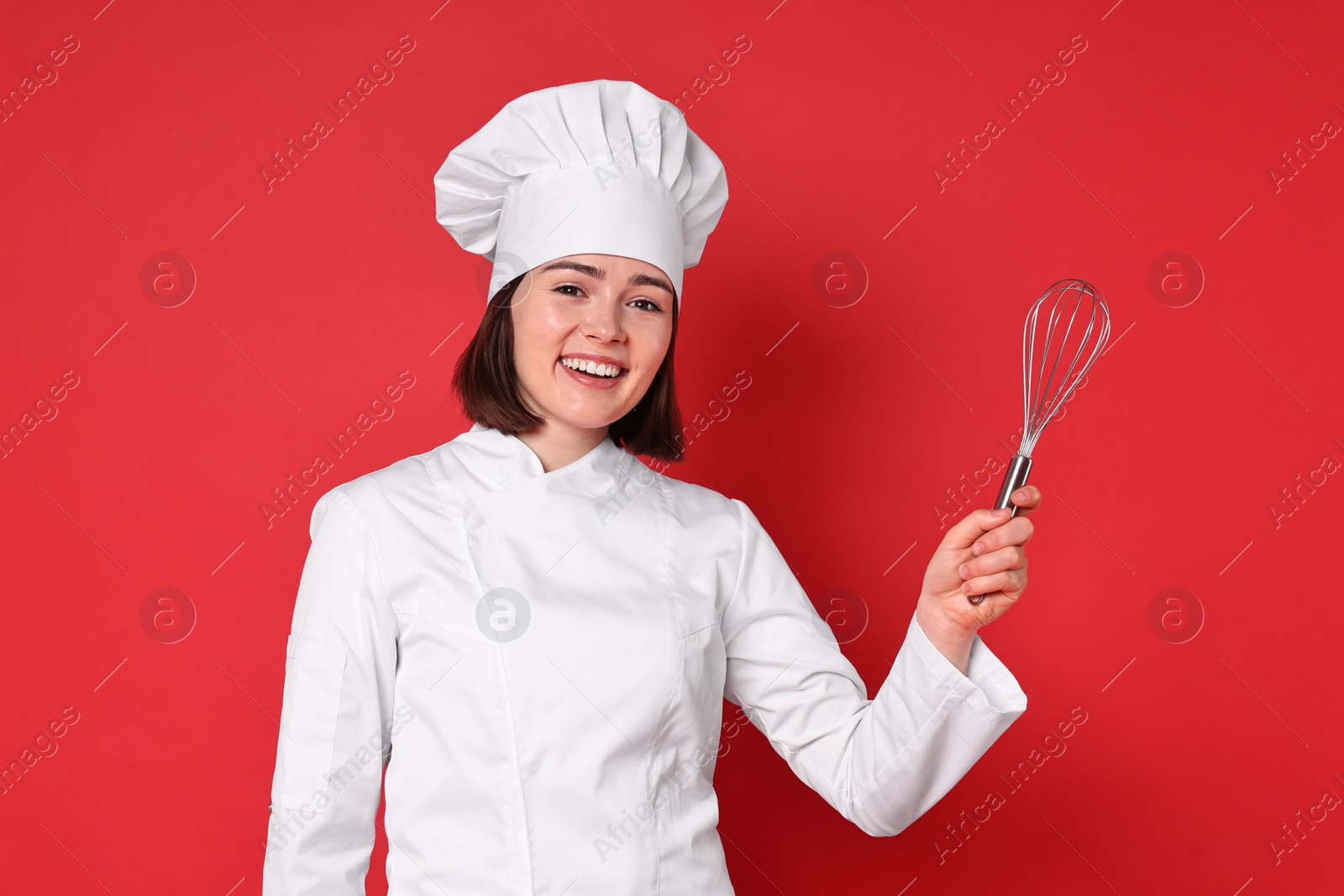 Photo of Happy confectioner holding whisk on red background