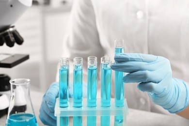 Photo of Scientist taking test tube with light blue liquid in laboratory, closeup