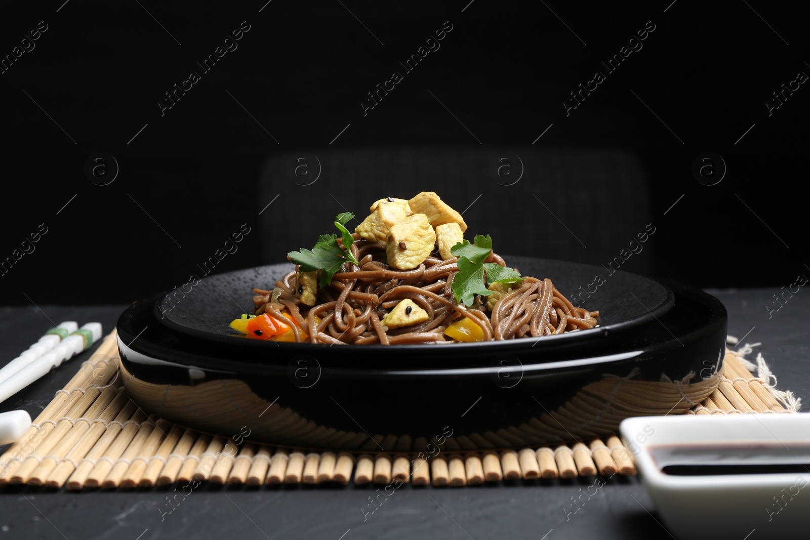 Photo of Stir-fry. Tasty noodles with meat and vegetables served on dark textured table