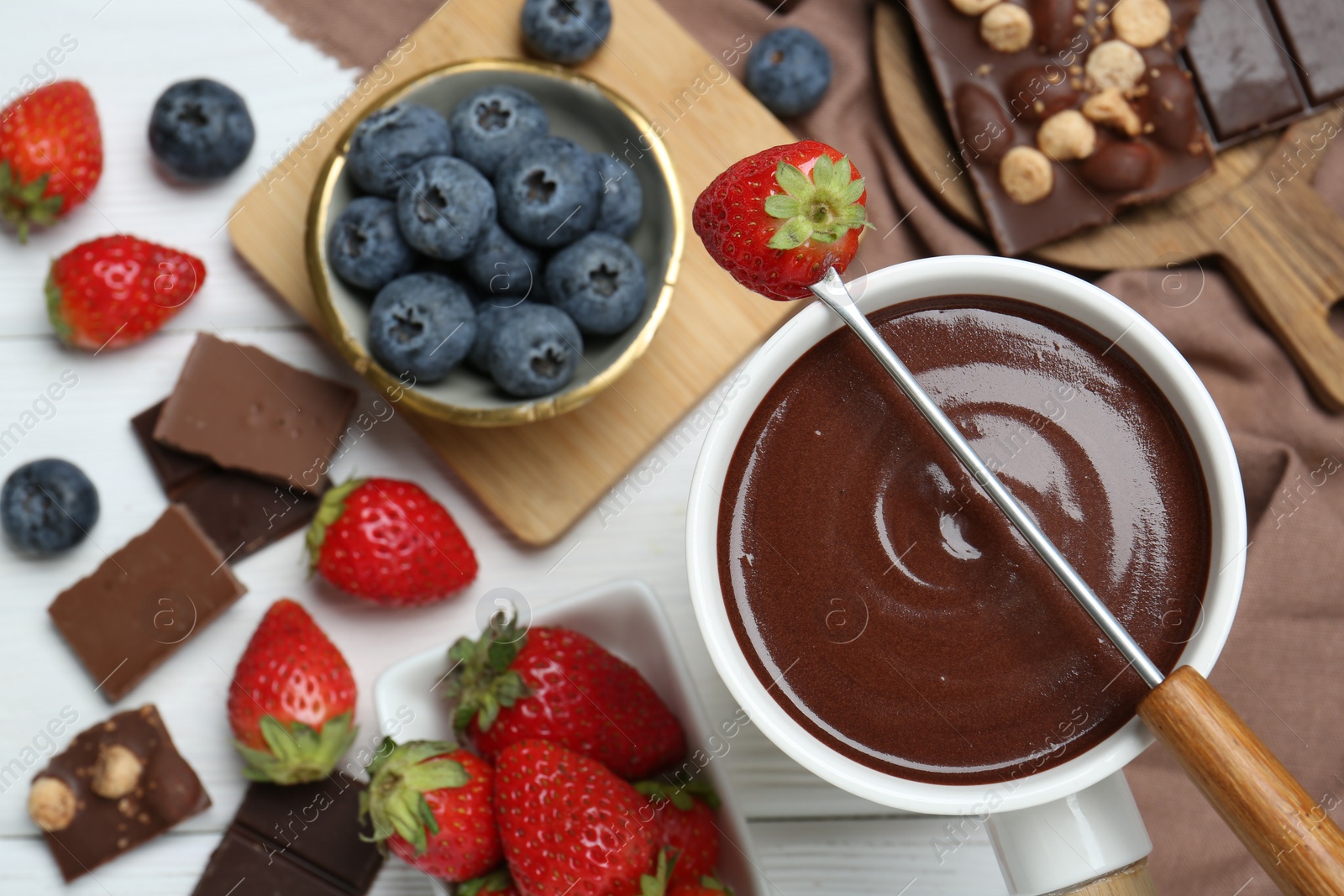 Photo of Fondue pot with chocolate, different berries and fork on white wooden table, flat lay