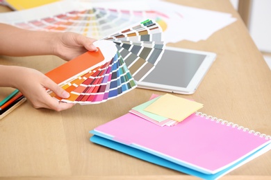 Photo of Designer with paint color palette samples at table, closeup
