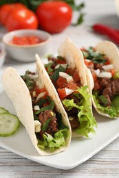 Photo of Delicious tacos with meat and vegetables on wooden table, closeup