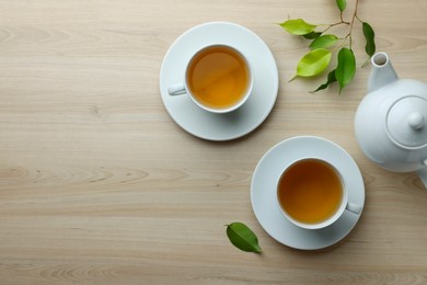 Green tea in white cups with leaves and teapot on wooden table, flat lay. Space for text