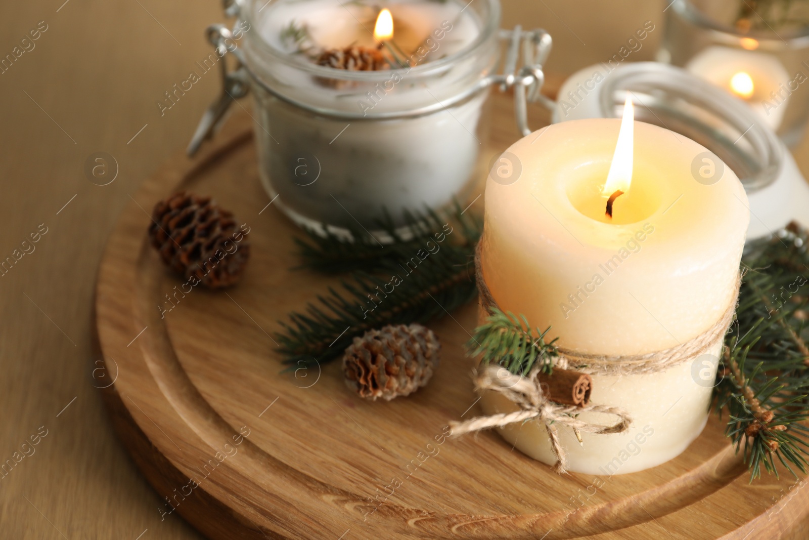 Photo of Burning scented conifer candles and Christmas decor on wooden table, closeup