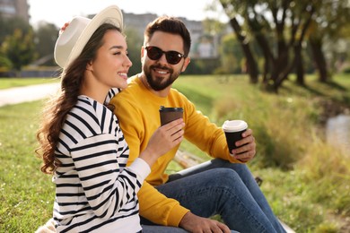 Photo of Beautiful young couple with takeaway coffee spending time together near pond in park