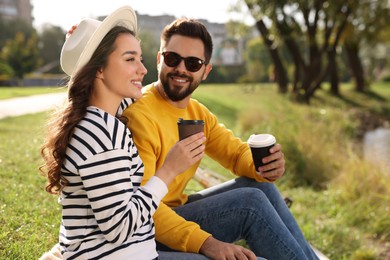 Beautiful young couple with takeaway coffee spending time together near pond in park