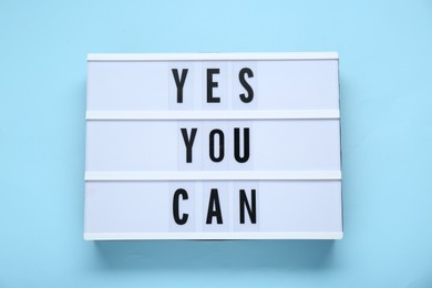 Lightbox with phrase Yes You Can on light blue background, top view. Motivational quote