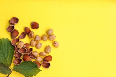 Photo of Tasty organic hazelnuts and leaves on yellow background, flat lay. Space for text