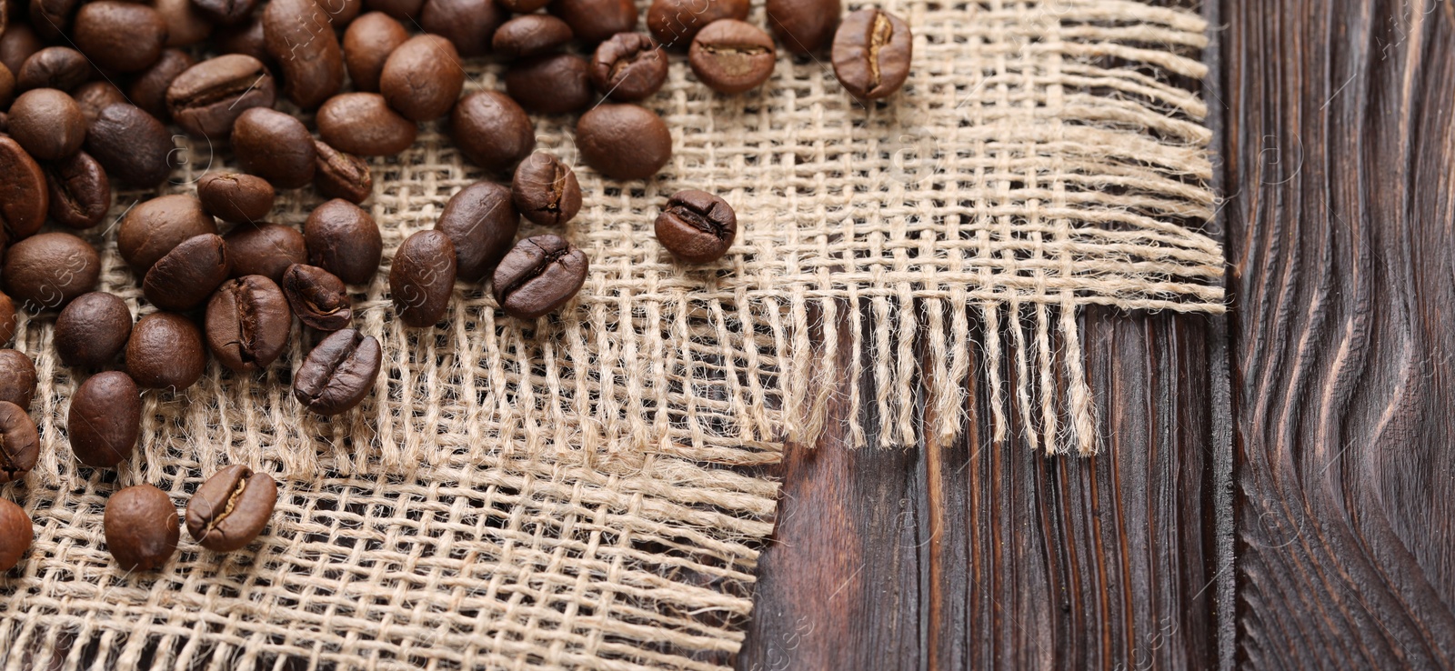 Photo of Many coffee beans and burlap fabric on wooden table, closeup. Space for text