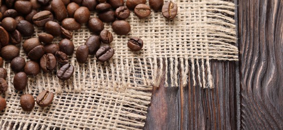 Photo of Many coffee beans and burlap fabric on wooden table, closeup. Space for text