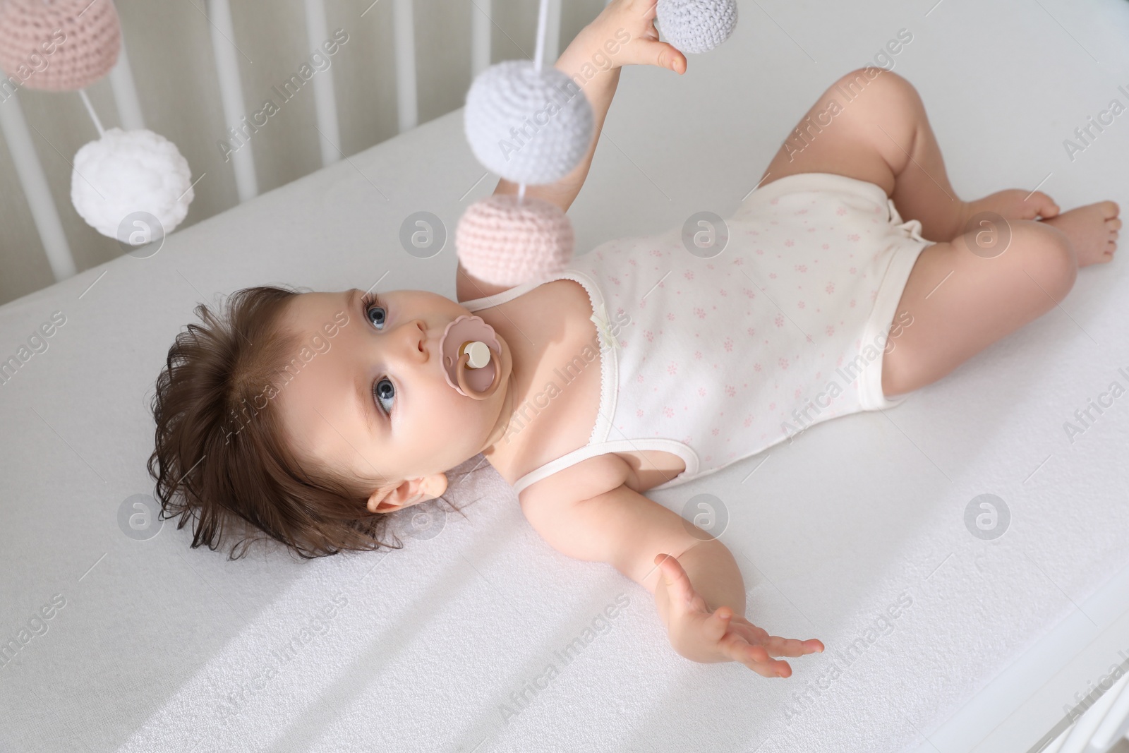 Photo of Cute little baby looking at hanging mobile in crib