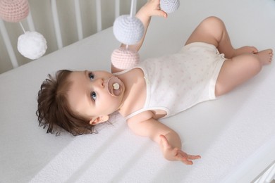 Photo of Cute little baby looking at hanging mobile in crib