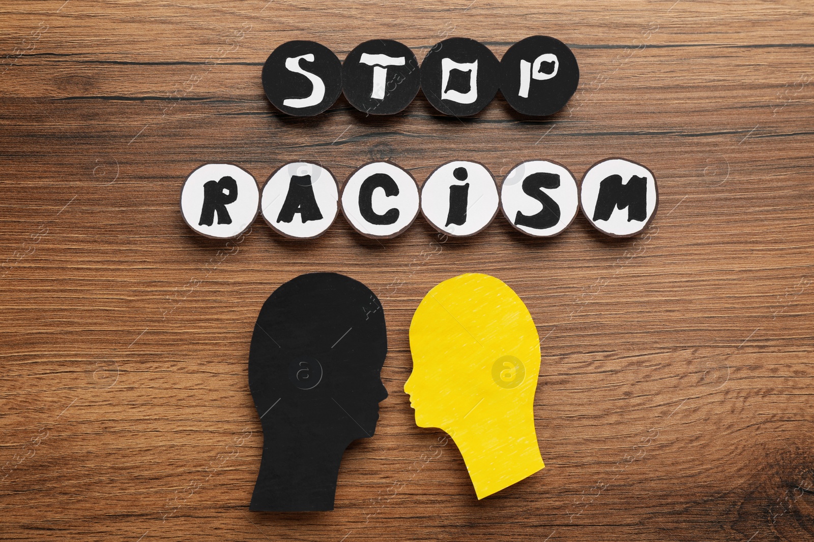 Photo of Phrase Stop Racism and different head cutouts on wooden table, flat lay