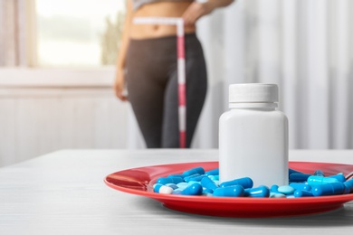 Photo of Plate of weight loss pills on table and woman with measuring tape indoors. Space for text