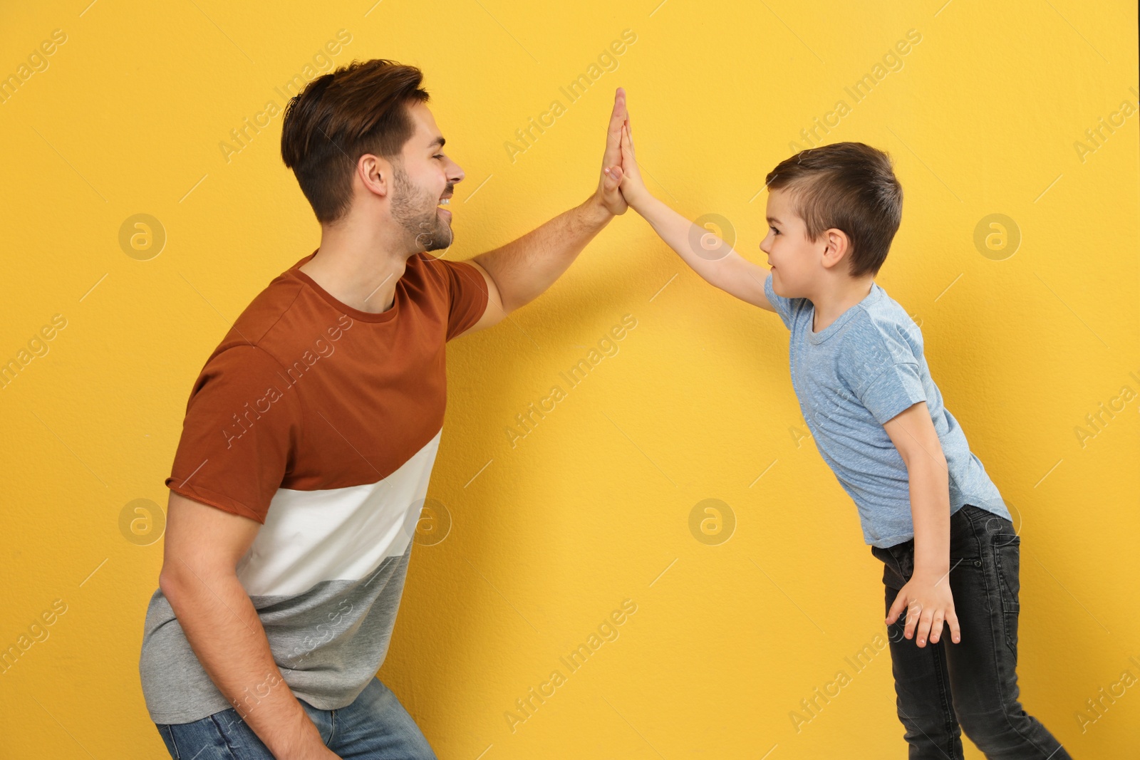 Photo of Portrait of dad and his son giving high five on color background