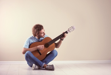 Photo of Young man playing acoustic guitar near grey wall. Space for text