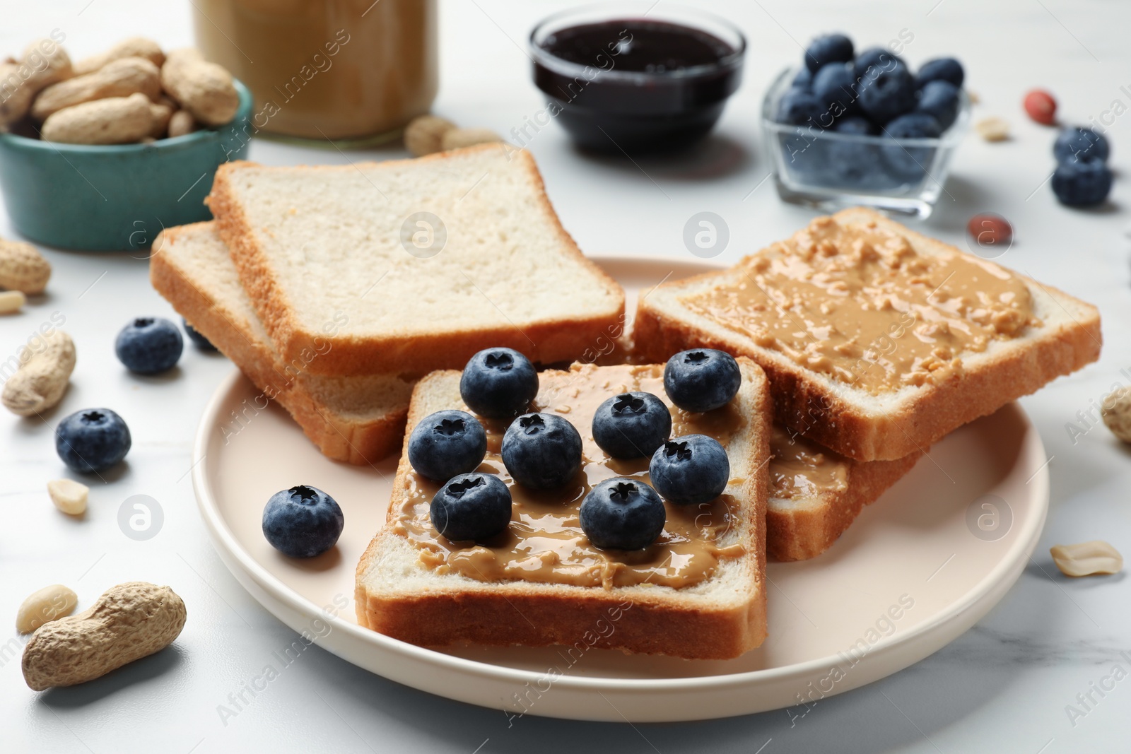 Photo of Delicious toasts with peanut butter and blueberries on white marble table, closeup