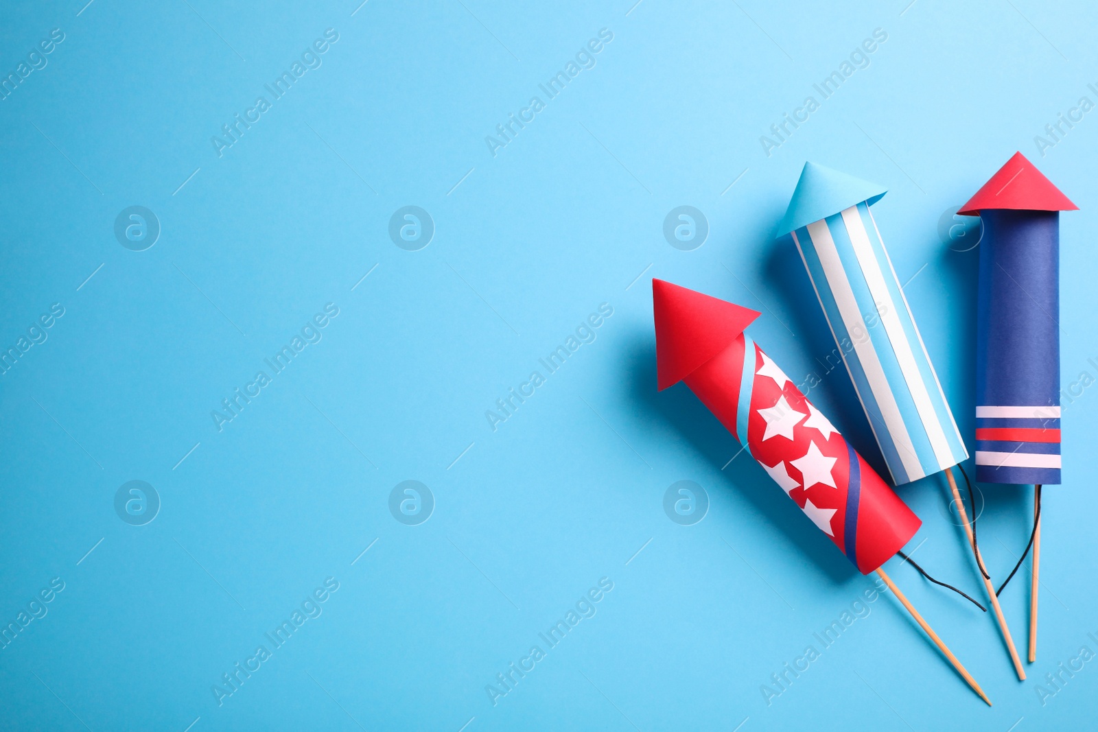 Photo of Firework rockets on light blue background, flat lay. Space for text