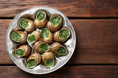 Delicious cooked snails on wooden table, top view. Space for text