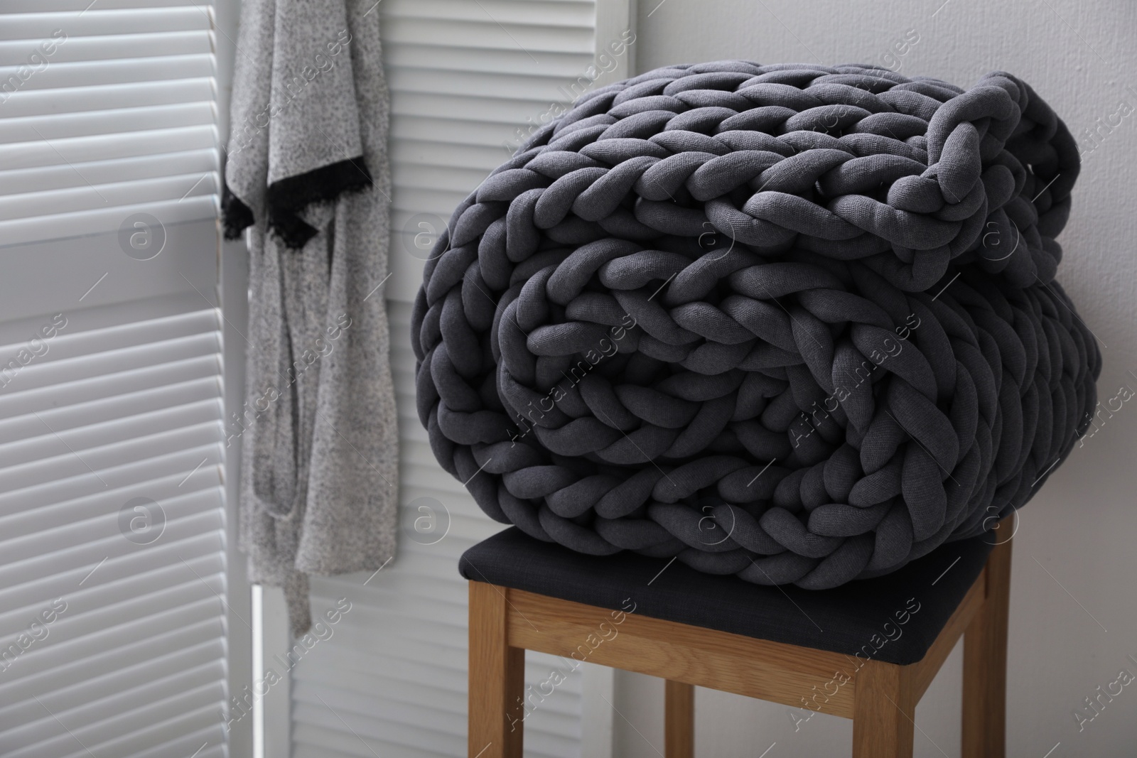 Photo of Dark grey chunky knit blanket rolled on wooden stool in room