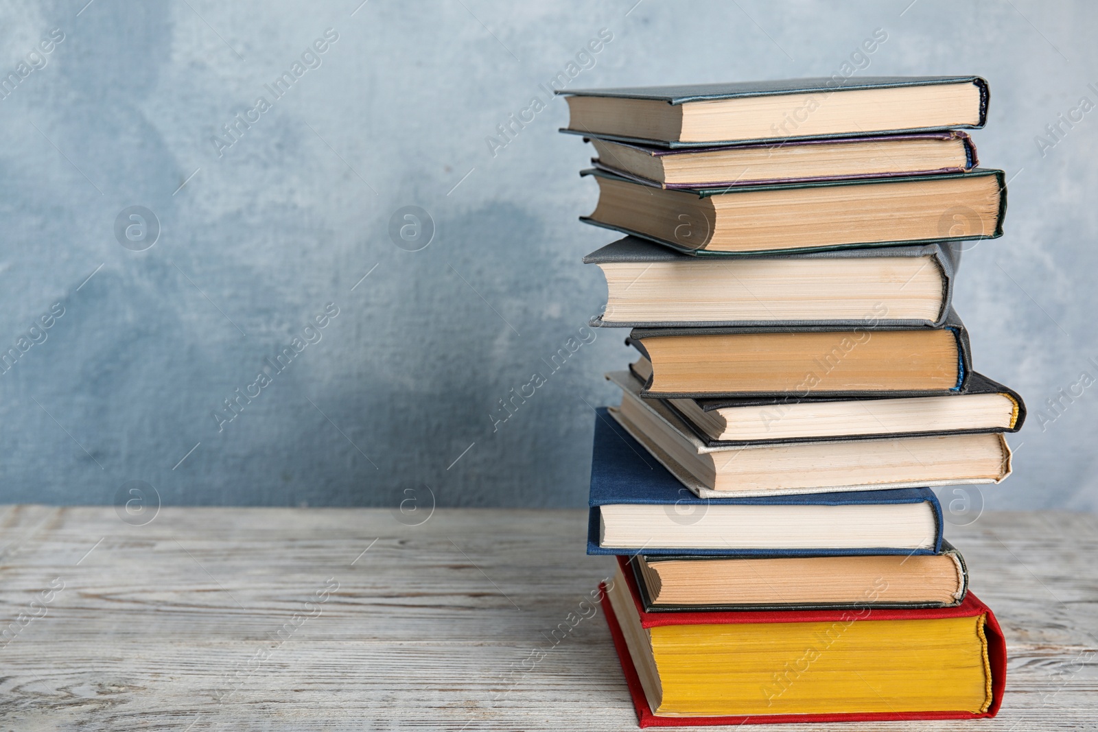 Photo of Stack of hardcover books on wooden table against light blue background. Space for text