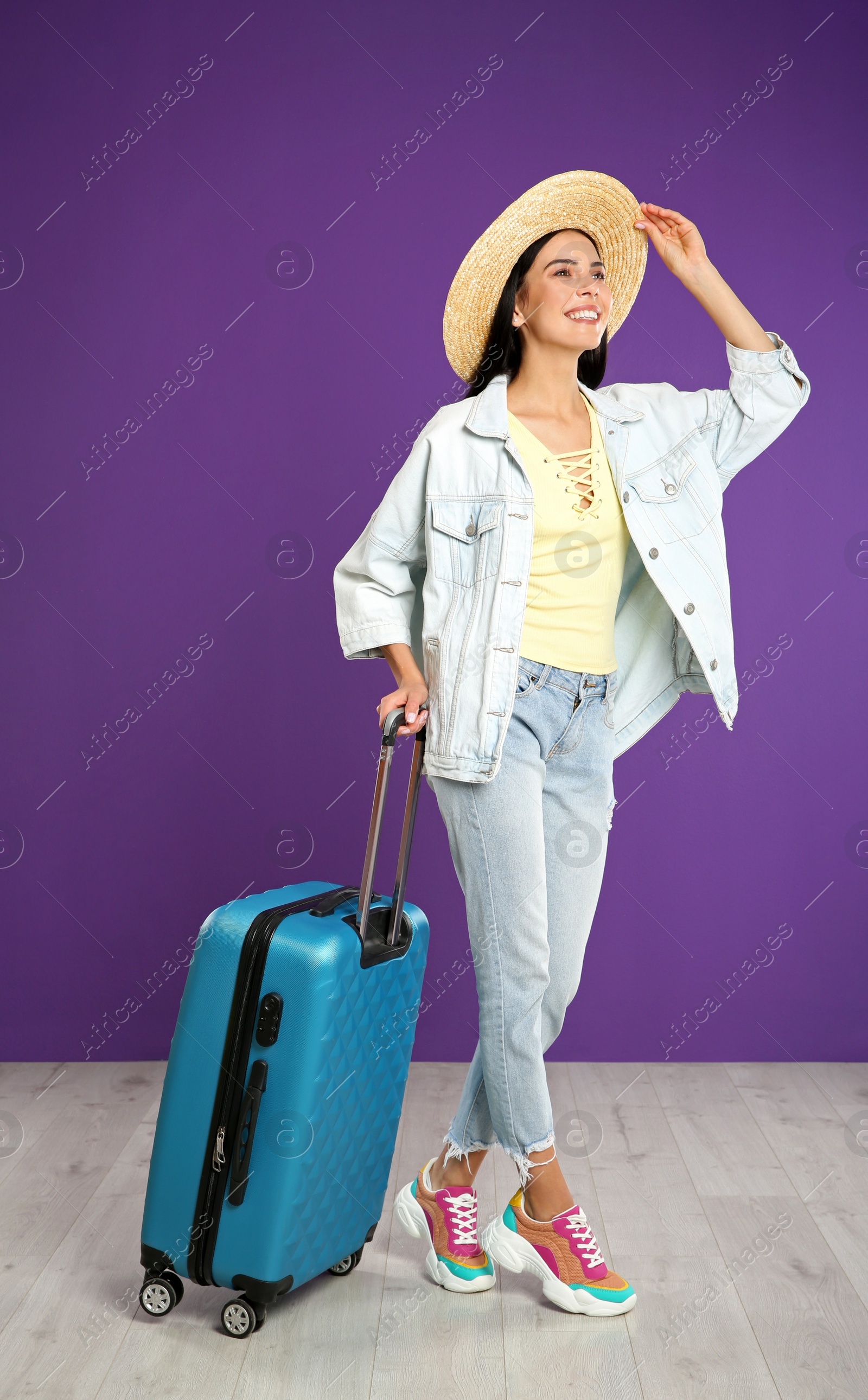 Photo of Beautiful woman with suitcase for summer trip near purple wall. Vacation travel