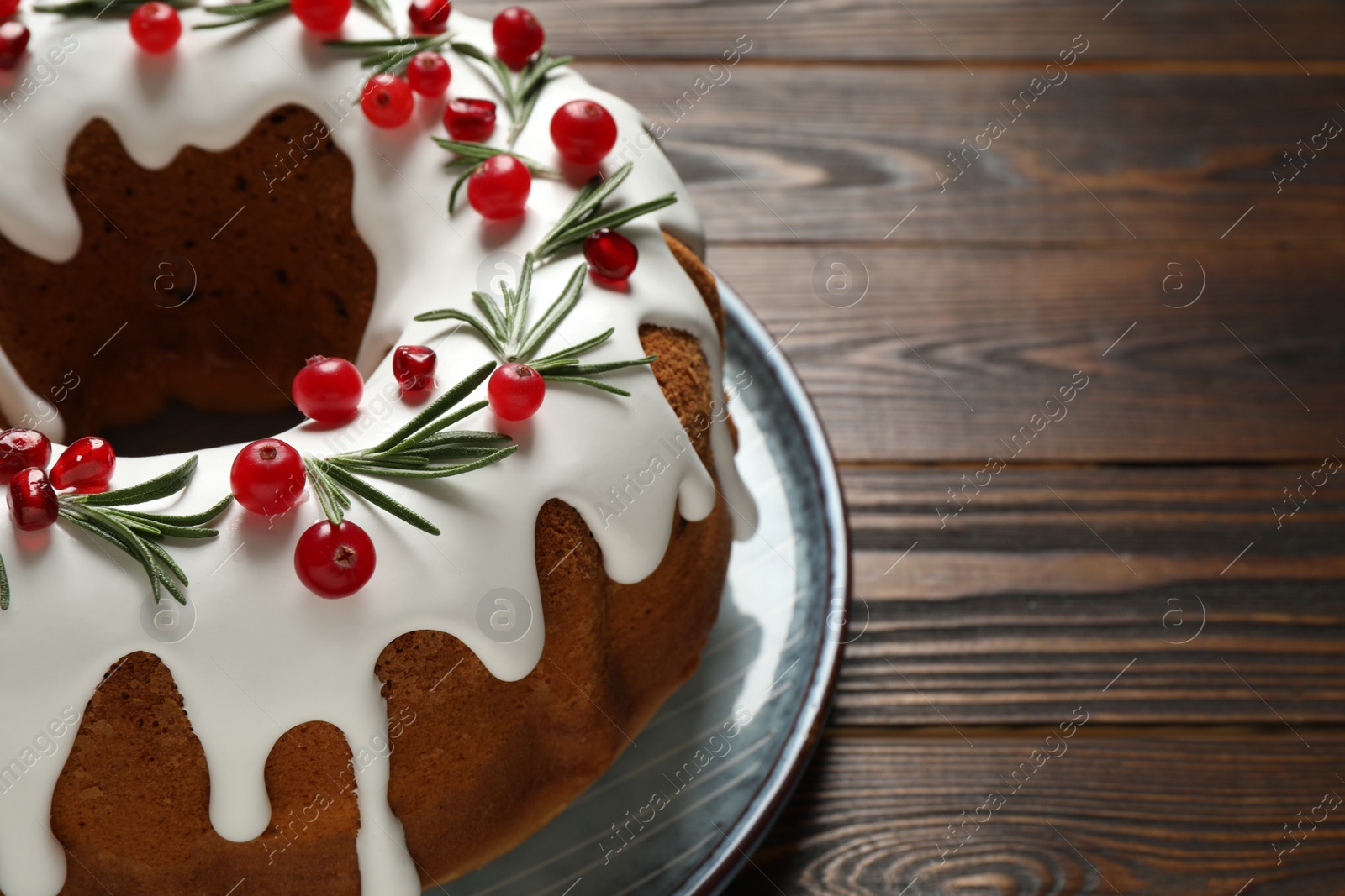 Photo of Traditional Christmas cake decorated with glaze, pomegranate seeds, cranberries and rosemary on wooden table, closeup. Space for text