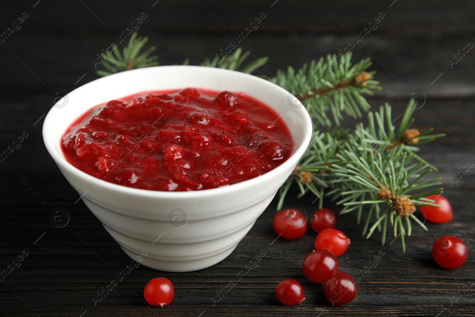 Photo of Bowl of cranberry sauce with fir tree branches on wooden background, closeup