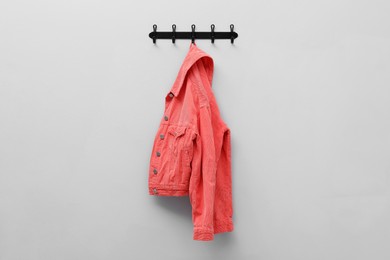 Coral jacket hanging on coat rack on light grey wall