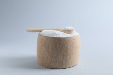 Photo of Organic white salt in bowl and spoon on light grey background, closeup