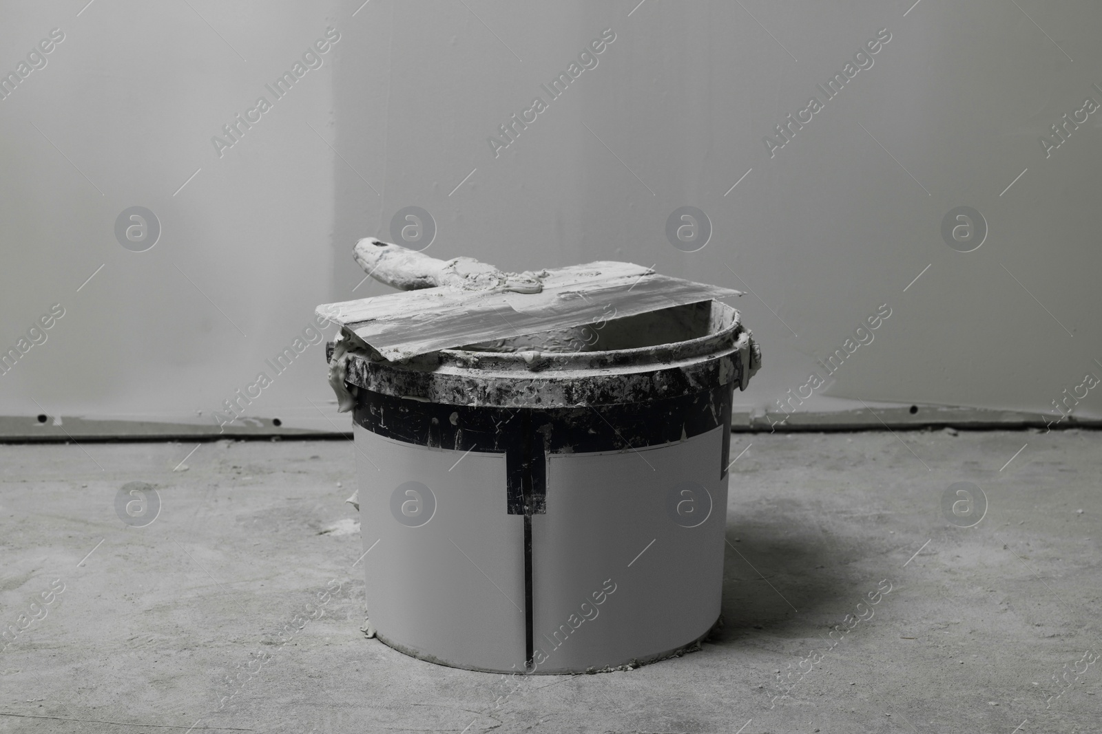 Photo of Bucket with plaster and putty knife near wall indoors