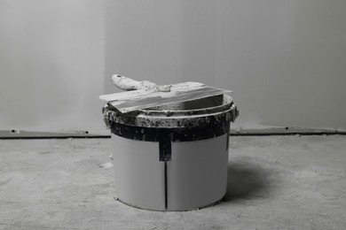Photo of Bucket with plaster and putty knife near wall indoors