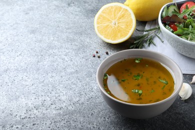 Bowl with lemon dressing near salad on grey table, space for text. Delicious salad dressing