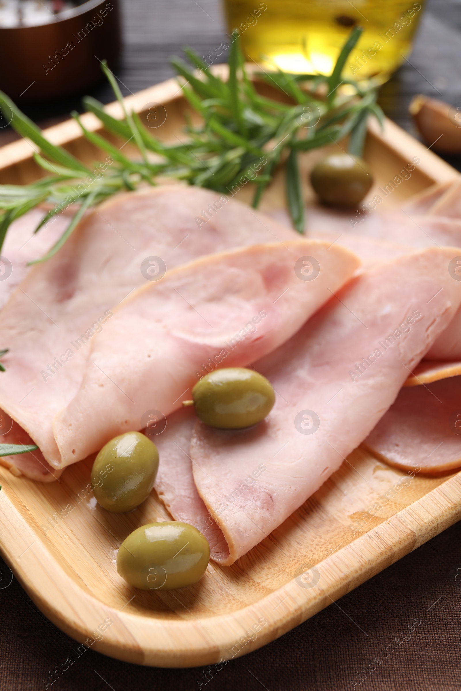 Photo of Slices of delicious ham with rosemary and olives on table, closeup