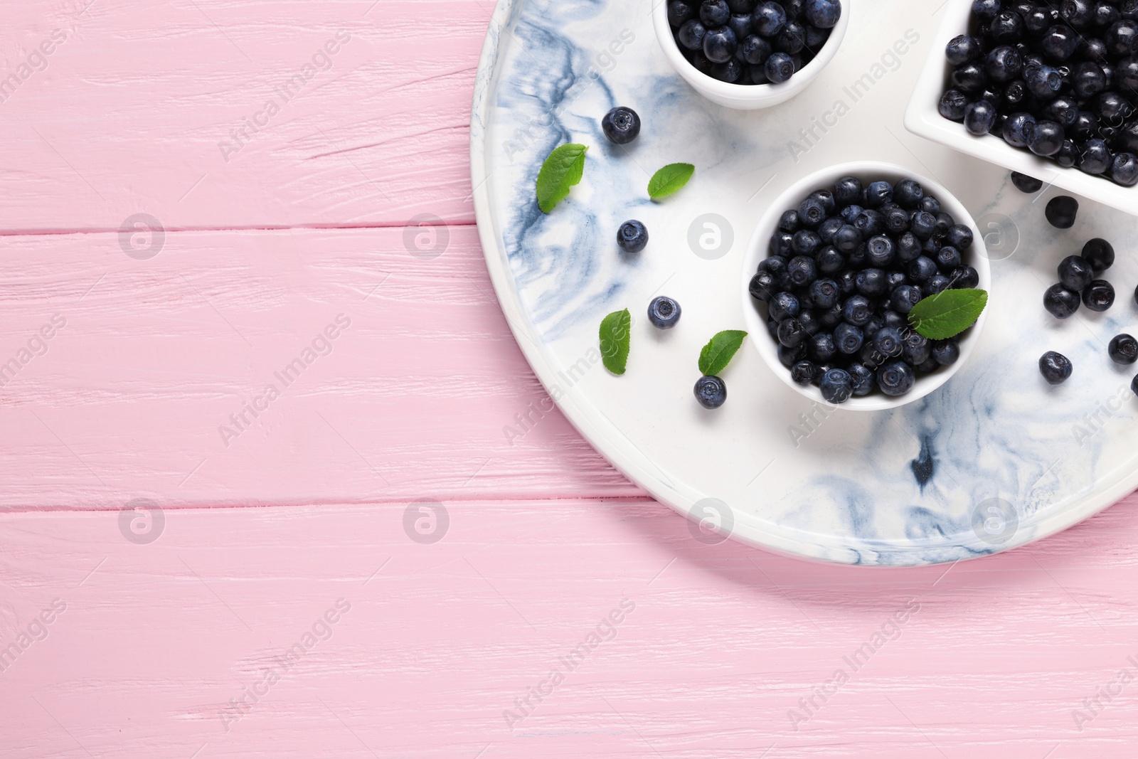 Photo of Bowls with tasty fresh bilberries and green leaves on pink wooden table, top view. Space for text