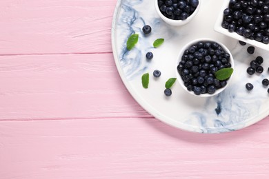 Bowls with tasty fresh bilberries and green leaves on pink wooden table, top view. Space for text