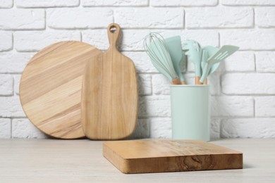 Different cutting boards and kitchen utensils in holder on light table near white brick wall